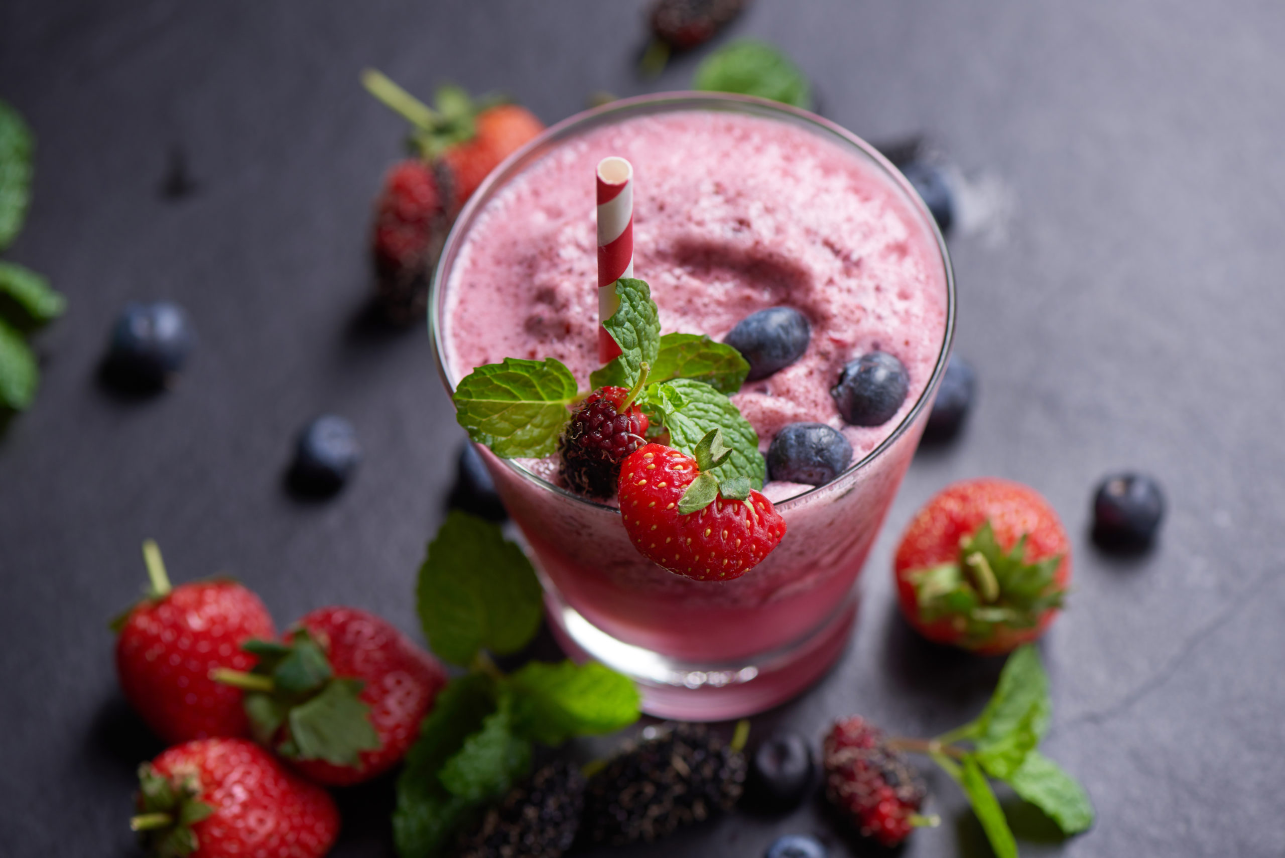 Delicious strawberry, mulberry and blueberry smoothie garnished with fresh berries and mint in glass. soft focus. beautiful appetizer pink raspberries, well being and weight loss concept.